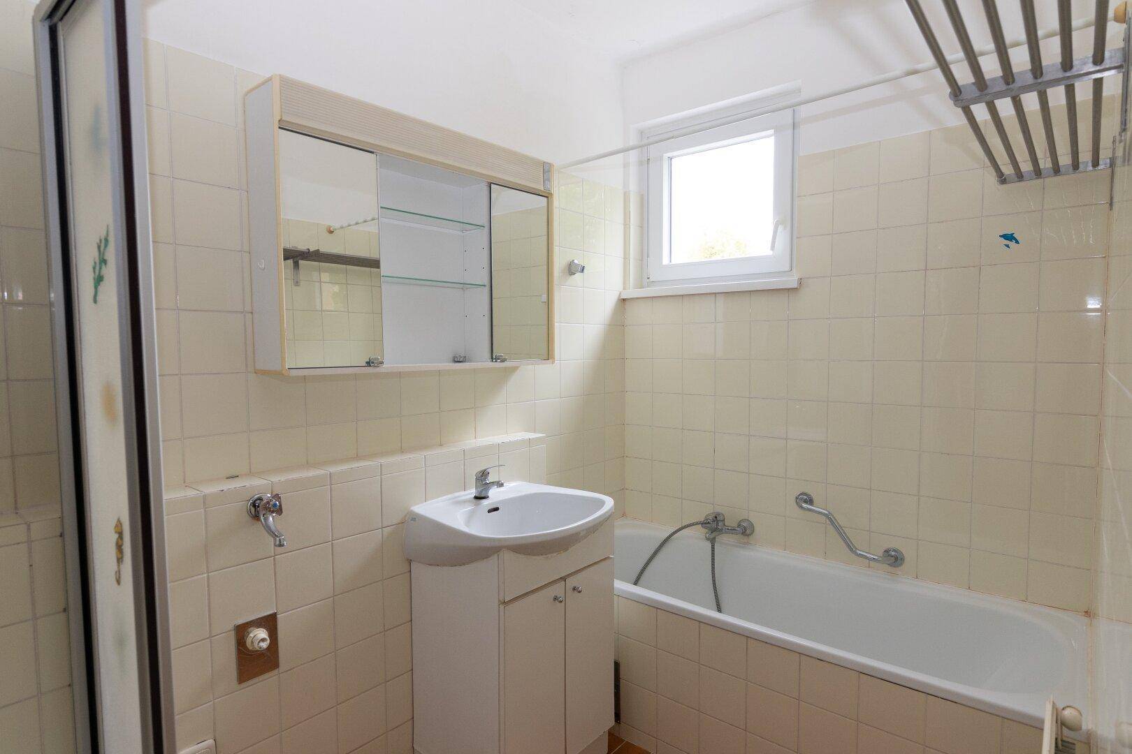 Badezimmer mit Badewanne, Waschbecken, Spiegelschrank und Fenster für Tageslicht.