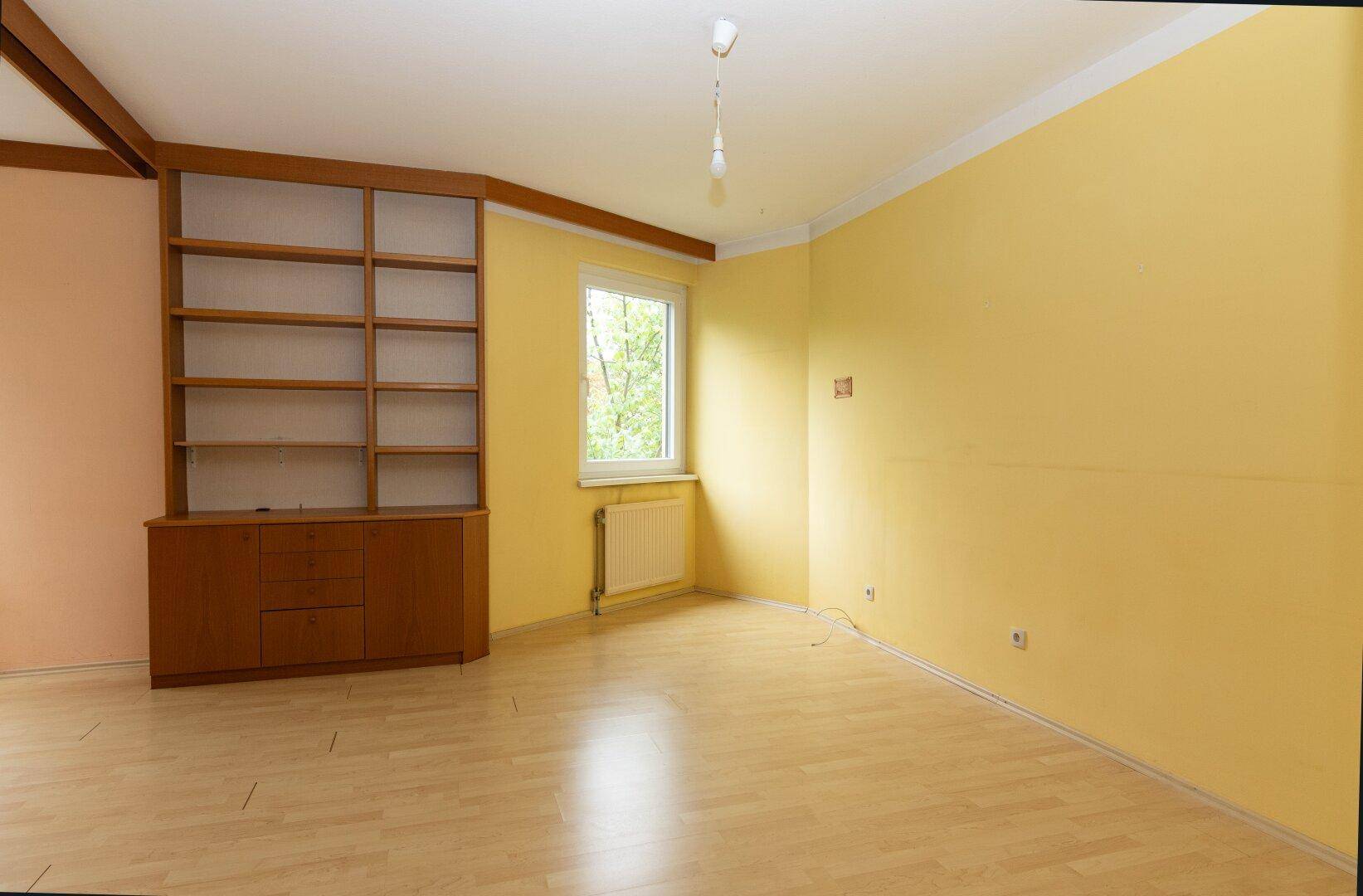 Geräumiges Zimmer mit Laminatboden, Holzdeckenbalken und gelb gestrichenen Wänden.
