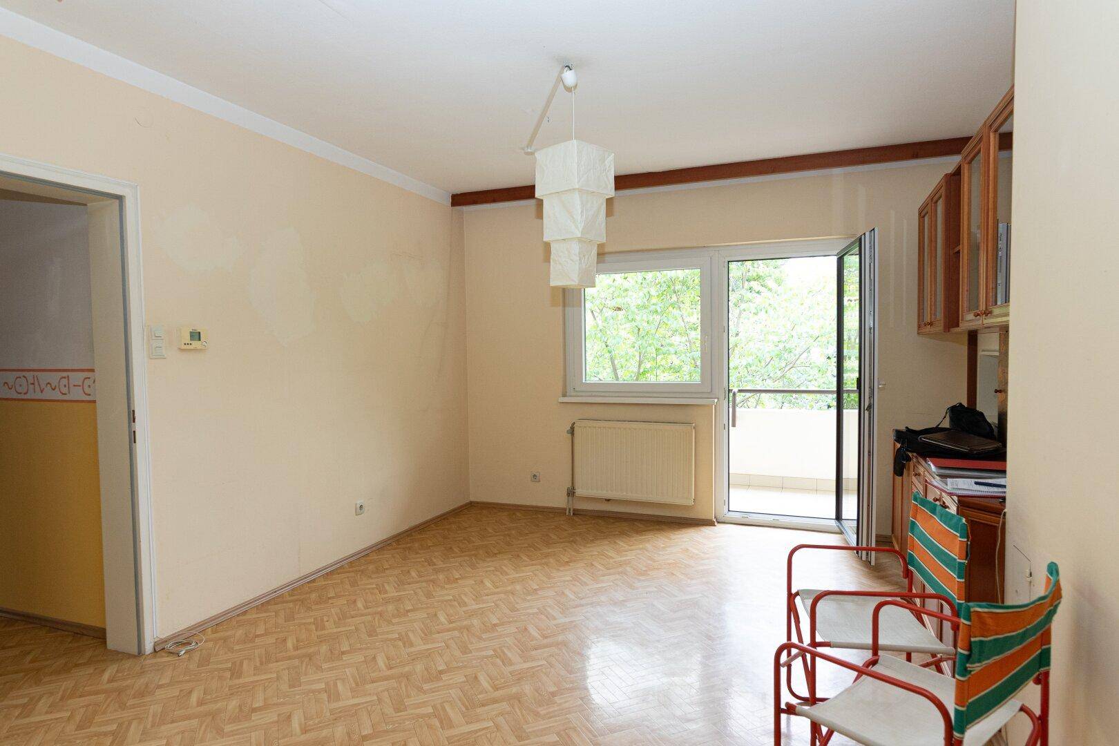 Helles Wohnzimmer mit Zugang zum Balkon, Laminatboden und einfacher Einrichtung.