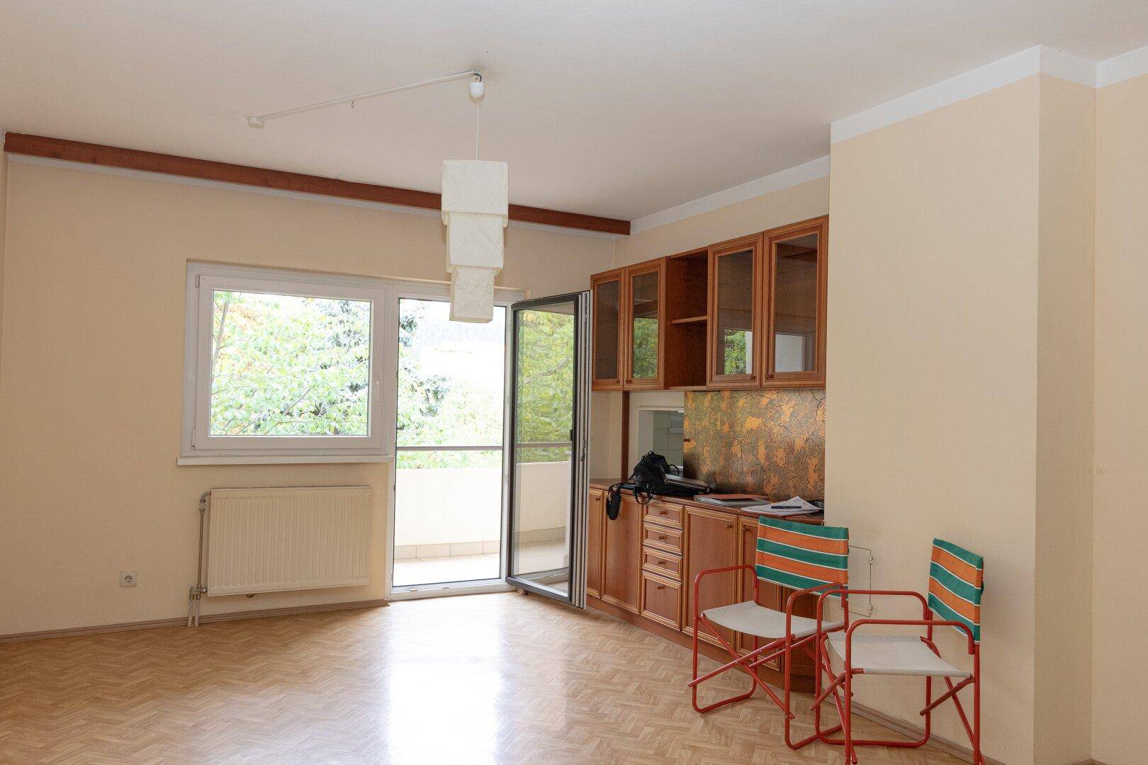 Wohnbereich mit Balkonzugang, Laminatboden und einem Holzschrank mit Glasfronten.