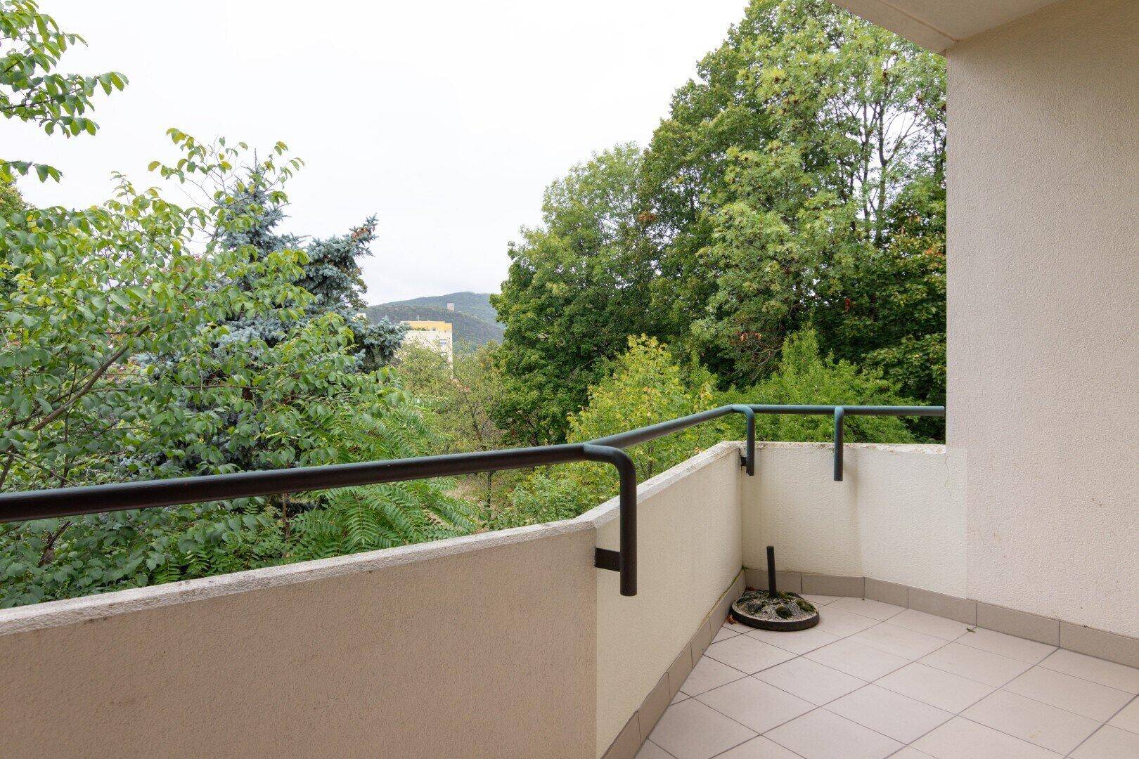 Balkon mit Fliesenboden und Blick ins Grüne, umgeben von Bäumen und Hügeln.