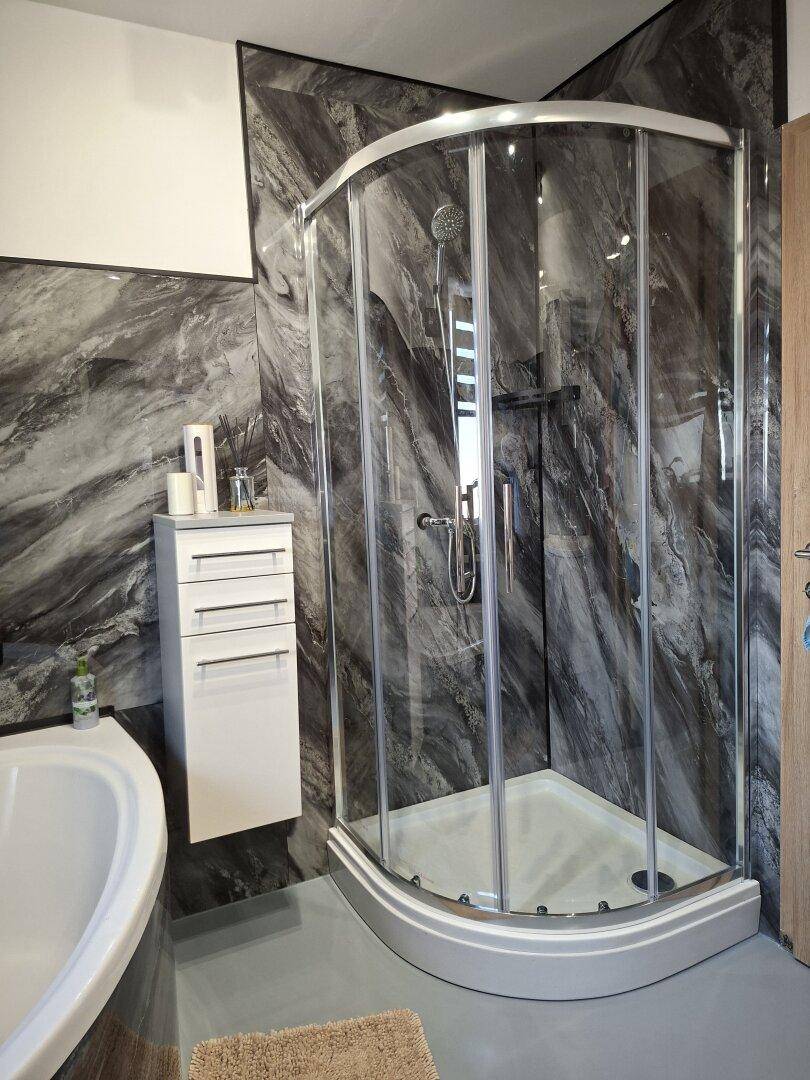 Modernes Badezimmer mit eleganter Duschkabine, Wänden in Marmoroptik und weißem Waschtischunterschrank.