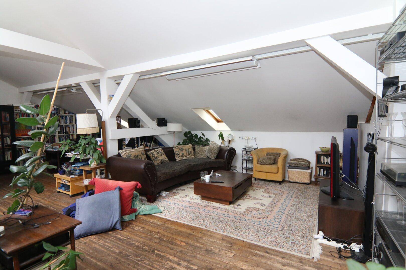 Gemütliches Wohnzimmer in einer Dachgeschosswohnung mit bequemer Couch, Teppich und Holzboden.