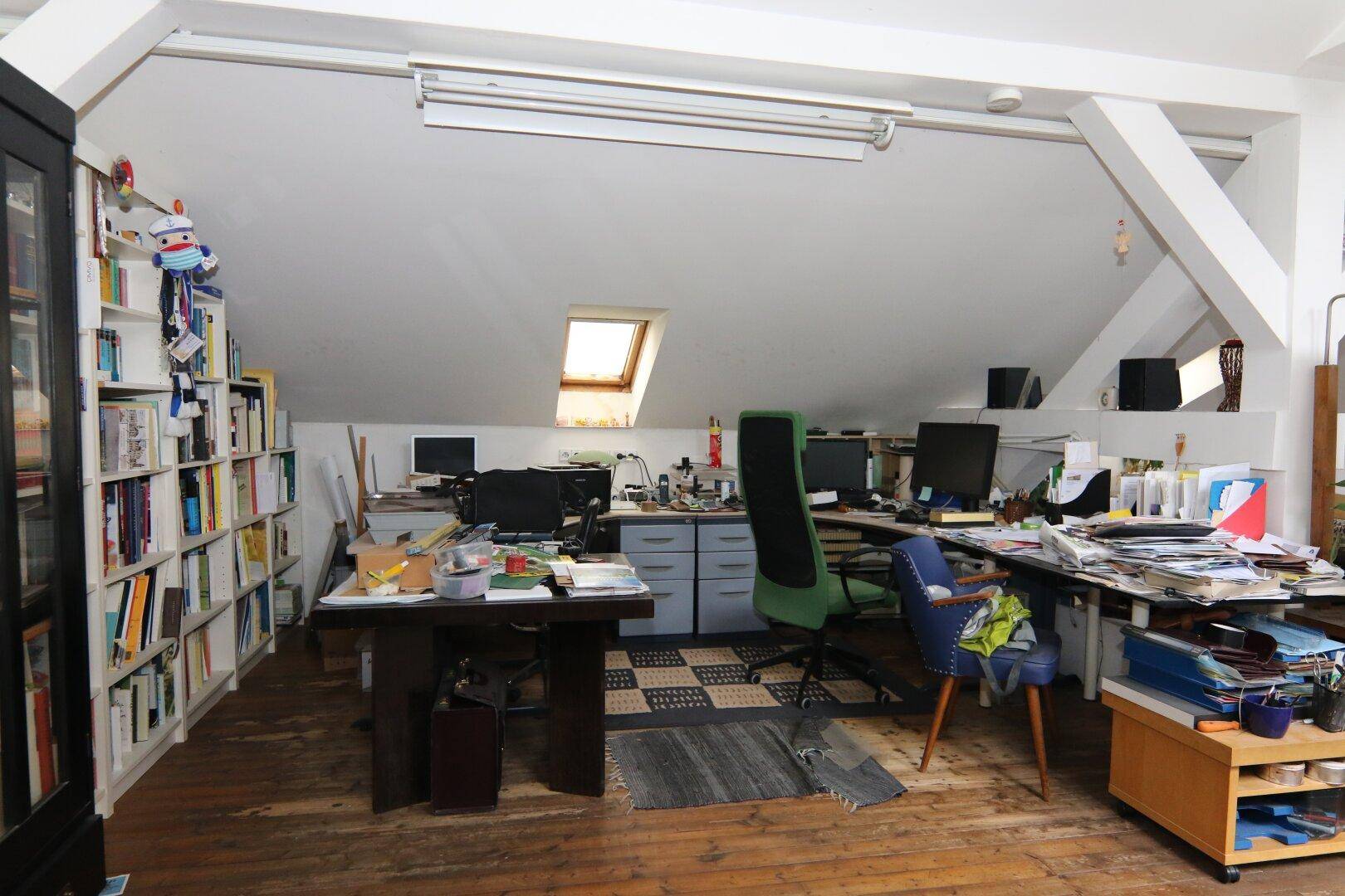 Helles Arbeitszimmer in einer Dachgeschosswohnung mit mehreren Schreibtischen, Bücherregalen und Holzboden.