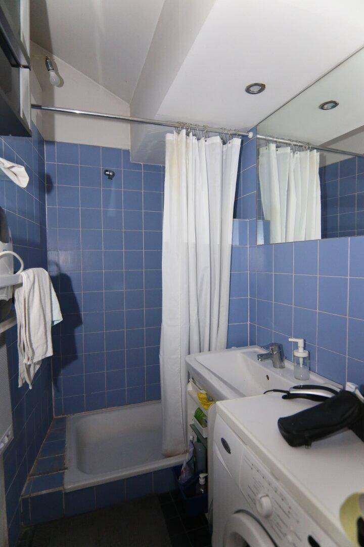 Badezimmer mit blauen Fliesen, Badewanne mit Duschvorhang, Waschbecken und Waschmaschine.