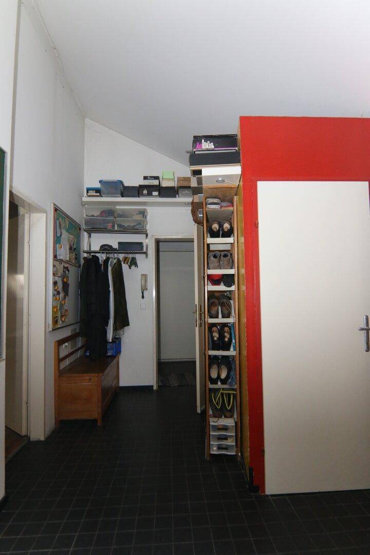 Eingangsbereich mit dunklem Fliesenboden, Garderobe, Schuhregal und rotem Akzent.