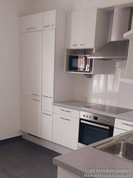 Moderne Einbauküche mit weißen Schränken, integrierter Mikrowelle und Dunstabzugshaube.