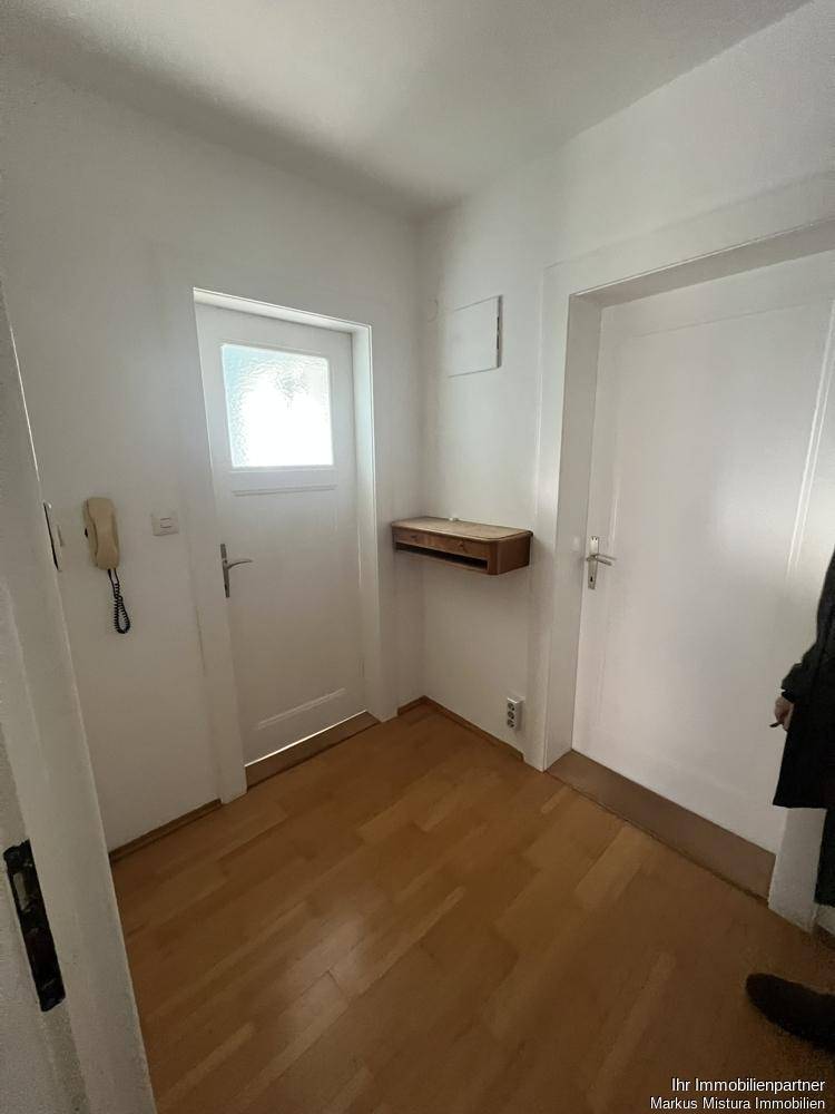 Heller Eingangsbereich mit Holzboden, weißer Tür und Gegensprechanlage.