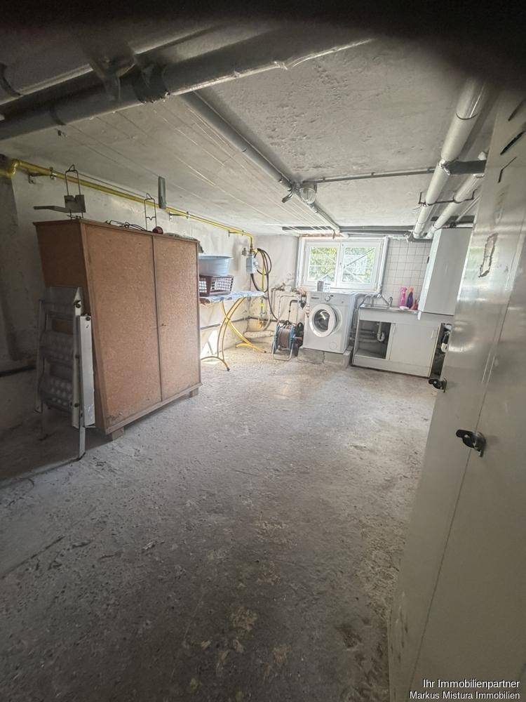 Waschküche im Keller mit Waschmaschine, Spülbecken und Fenster.