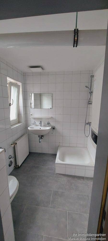 Gefliestes Badezimmer mit Badewanne, Dusche, Waschbecken und Fenster für natürliche Belüftung.