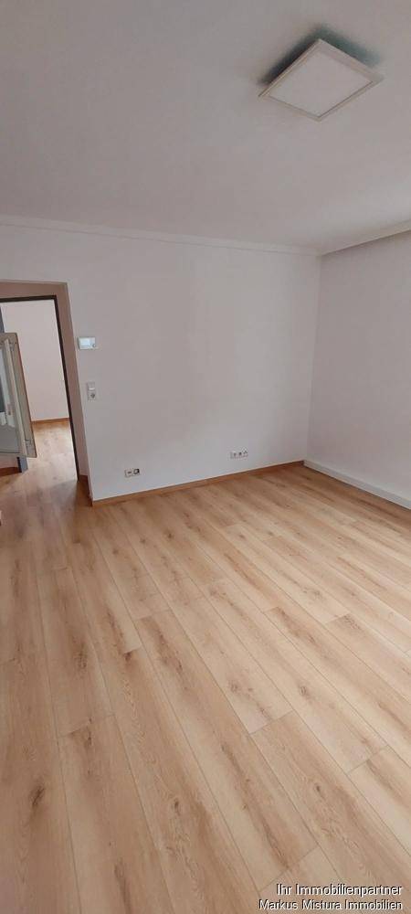 Heller Raum mit Laminatboden und weißen Wänden, der Zugang zu einem weiteren Bereich bietet.
