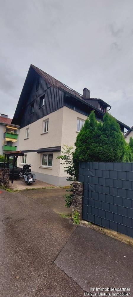 Außenansicht eines Hauses mit markantem Satteldach, heller Fassade und dunkler Holzverkleidung.
