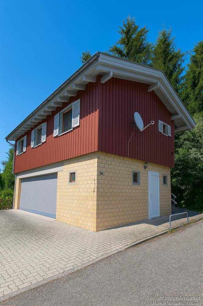 Charmantes Haus mit roter Holzfassade und gelbem Sockel, inklusive integrierter Garage und Satellitenschüssel.