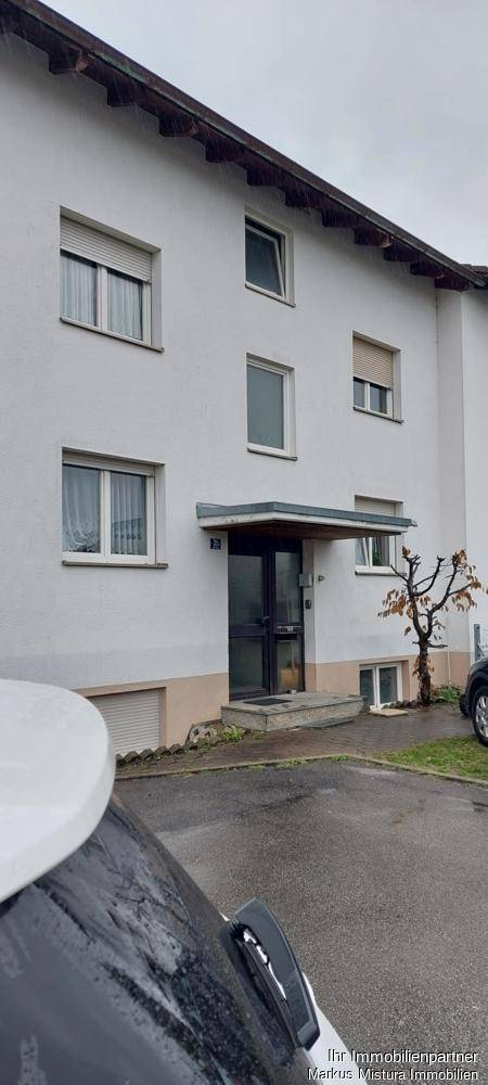 Fassade eines Mehrfamilienhauses mit mehreren Fenstern und Rollläden sowie einem Eingangsbereich.