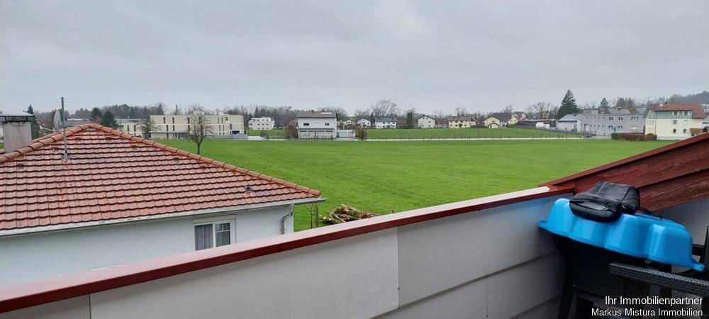 Panoramablick über weite grüne Flächen und Wohngebäude von einem Balkon aus.