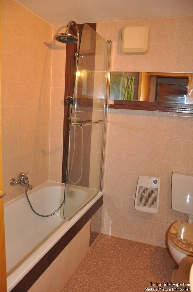 Badezimmer mit Badewanne, Duschvorrichtung, WC und beigefarbenen Fliesen an Wänden und Boden.