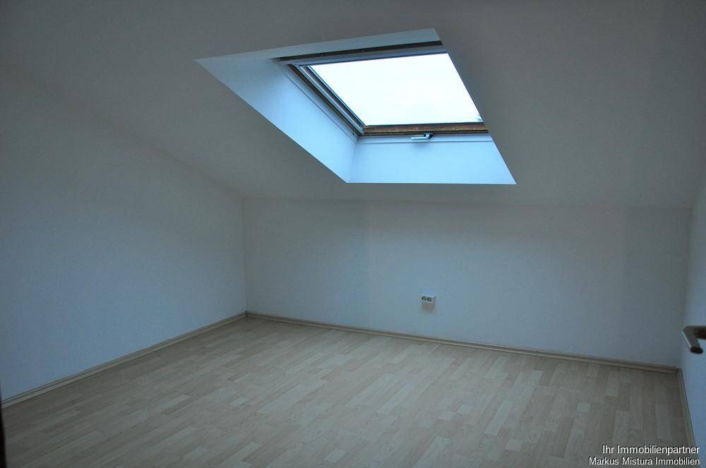 Helles Zimmer im Dachgeschoss mit Laminatboden und einem großen Dachfenster für viel Tageslicht.