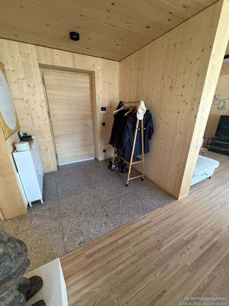 Heller Eingangsbereich mit Holzwänden, Fliesenboden und Garderobenständer.