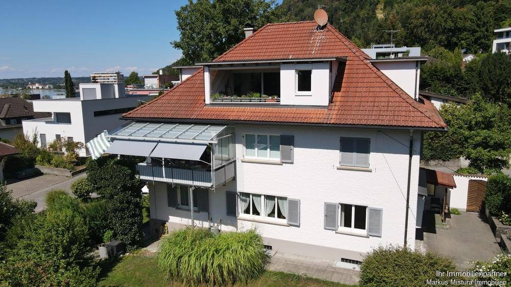 Ansicht des Hauses von einer anderen Perspektive, umgeben von Grünflächen und weiteren Gebäuden mit Seeblick.