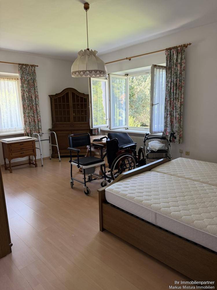 Helles Schlafzimmer mit Holzmöbeln, Parkettboden und großen Fenstern mit Blick ins Grüne.