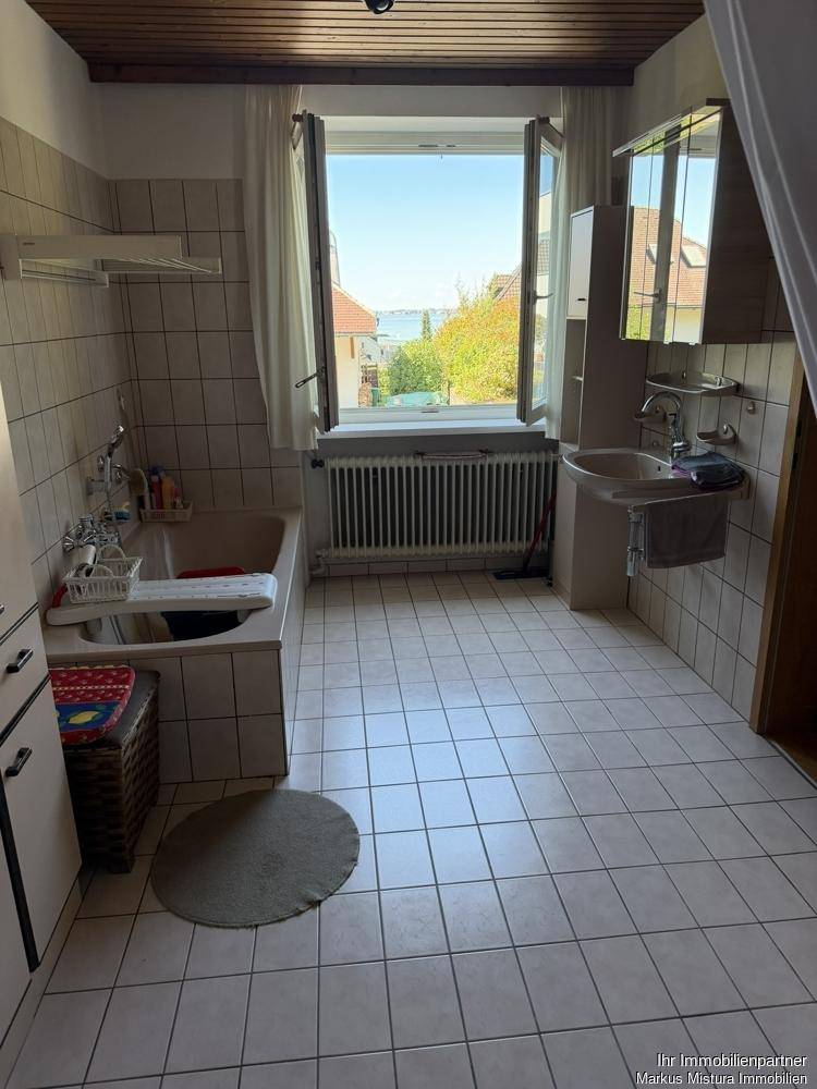 Badezimmer mit weißen Fliesen, Badewanne, Waschbecken und einem Fenster mit Seeblick.