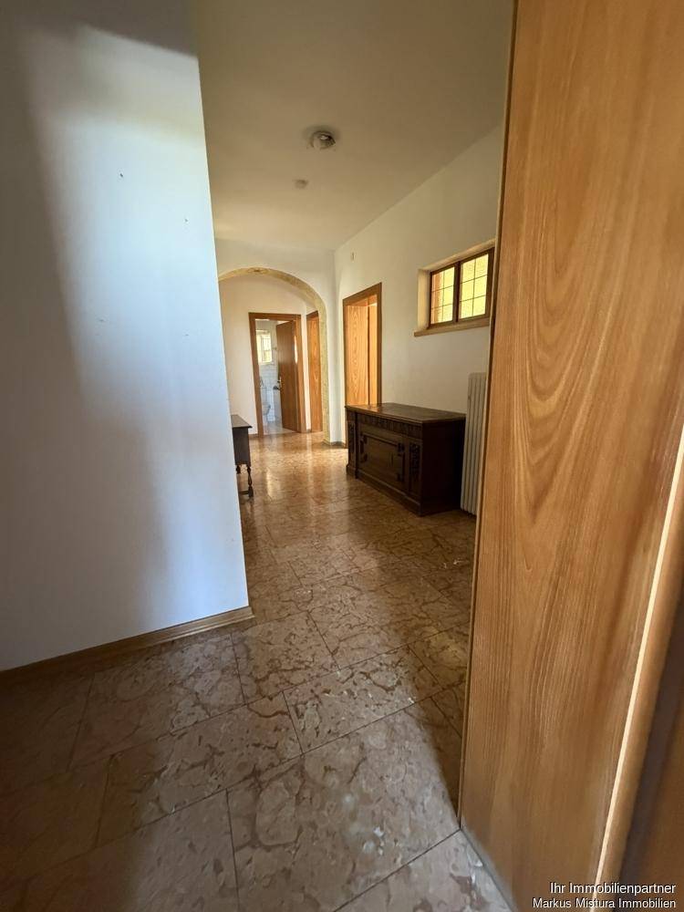 Langer Flur mit gemustertem Fliesenboden, Holztüren und einer Holzdecke, führt zu weiteren Räumen.