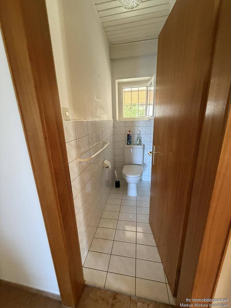 Kleines Gäste-WC mit weißen Fliesen, Toilette und einem Fenster für natürliche Belüftung.