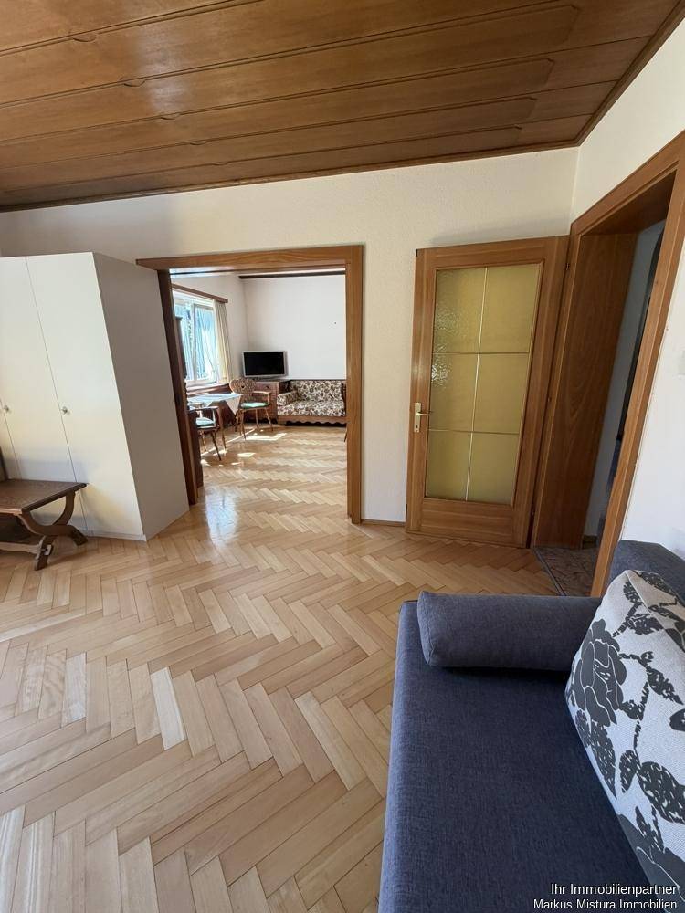 Blick vom Wohnzimmer in einen angrenzenden Raum, beide mit Fischgrätparkett und traditioneller Einrichtung.
