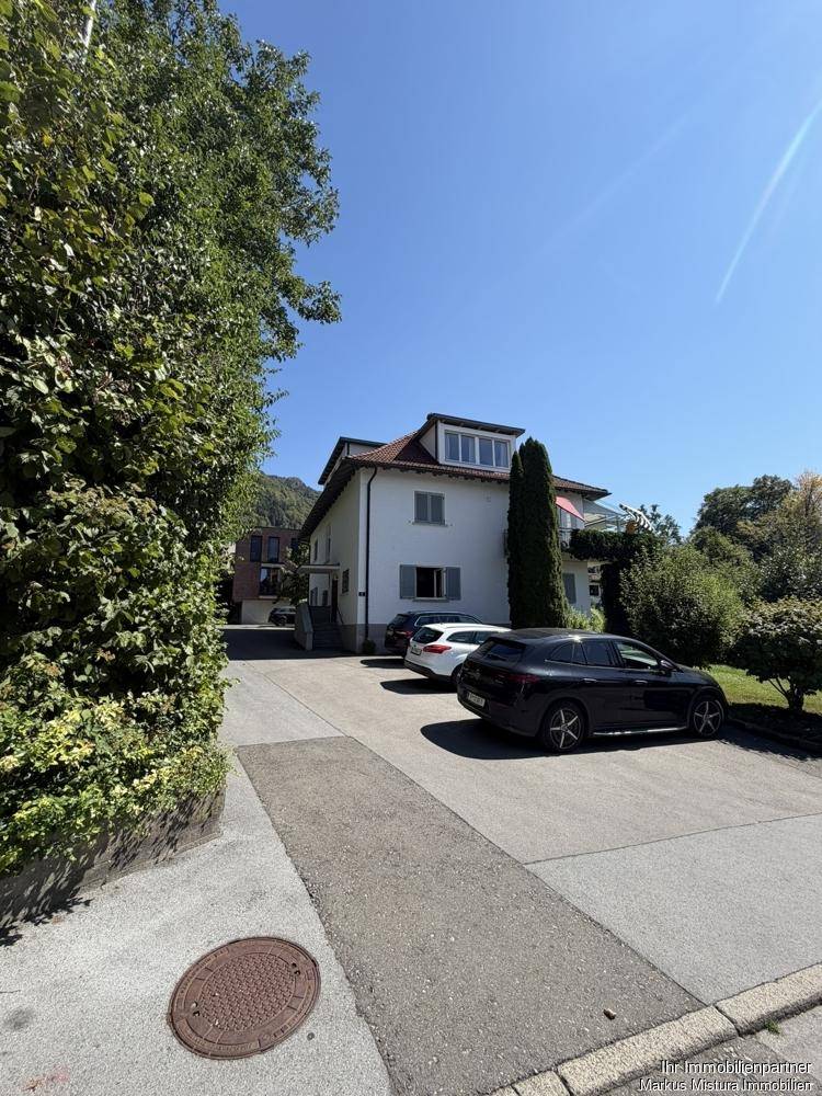 Straßenansicht des Hauses mit Einfahrt, geparkten Autos und einer grünen Hecke.