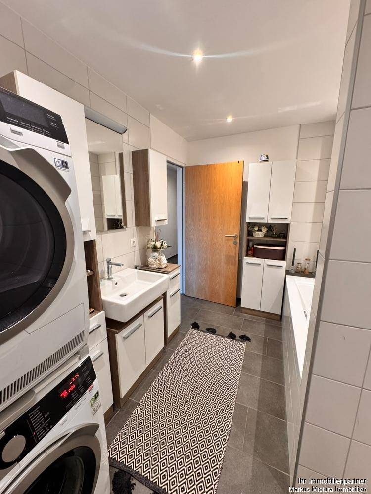 Modernes Badezimmer mit Waschbecken, Spiegelschrank, praktischen Schränken und integrierter Waschmaschine und Trockner.