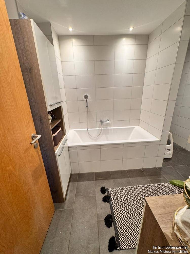 Helles Badezimmer mit einer Badewanne, weißen Wandfliesen und dunklem Boden, ideal zum Entspannen nach einem langen Tag.