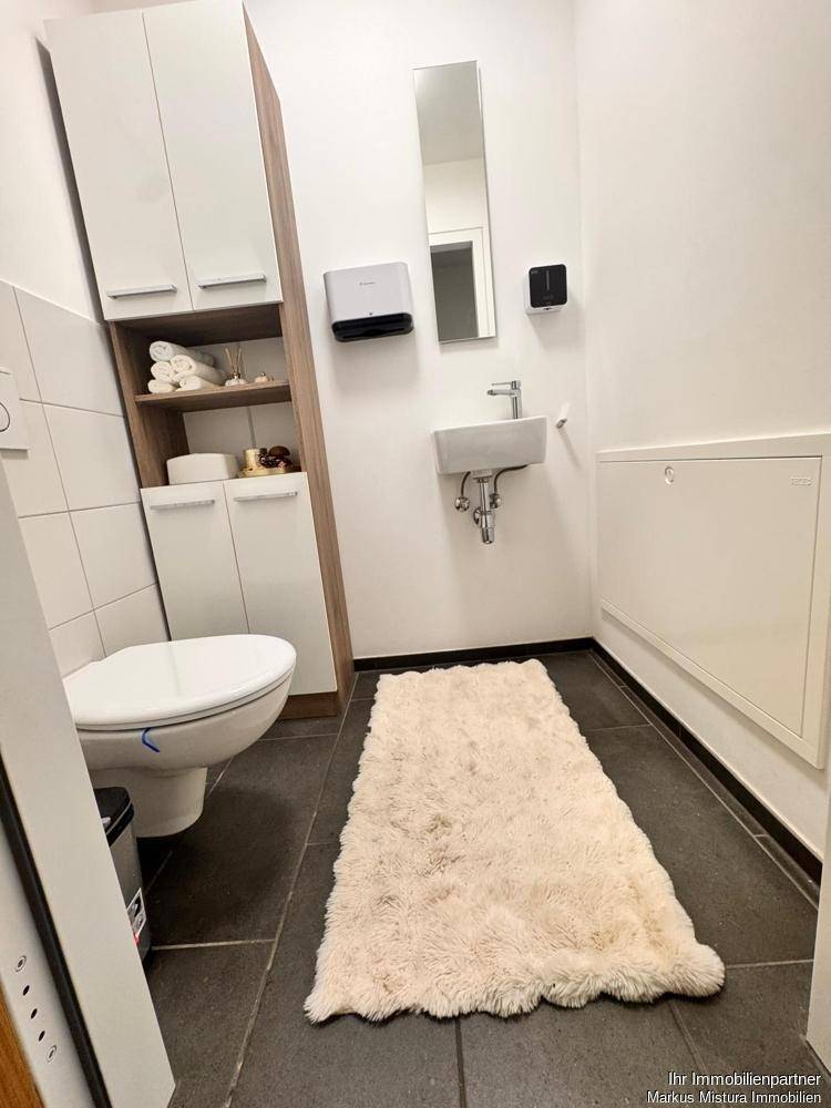 Kleines Gäste-WC mit wandhängender Toilette, Handwaschbecken, Spiegel und einem praktischen Hochschrank für Stauraum.