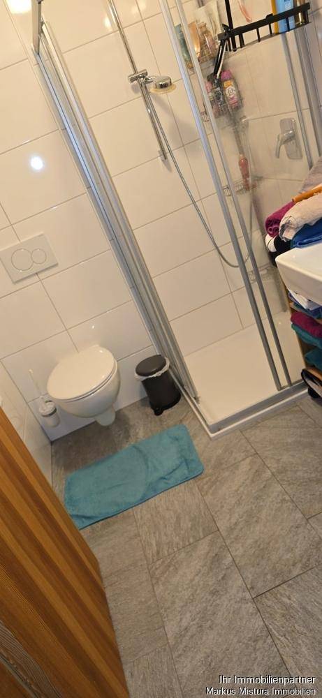Funktionales Badezimmer mit Duschkabine, Toilette und hellen Fliesen am Boden und an den Wänden.