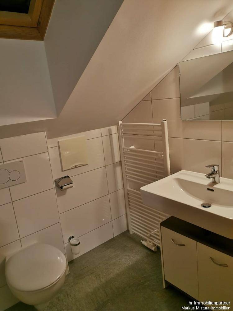 Helles Dachgeschoss-Badezimmer mit Toilette, Einzelwaschbecken, beheiztem Handtuchhalter und Dachfenster.