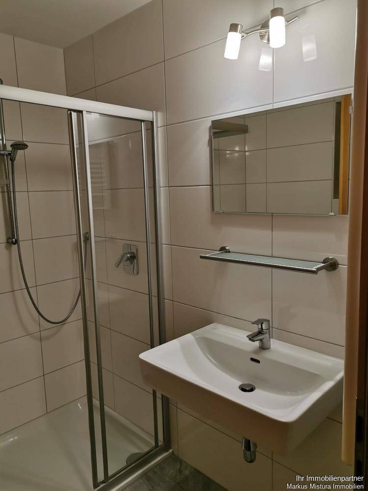Modernes Badezimmer mit Duschkabine, Einzelwaschbecken und hellen Fliesen an den Wänden.