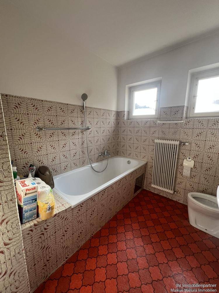 Badezimmer mit Badewanne, Duschfunktion und auffälligen Fliesen im Retro-Stil.