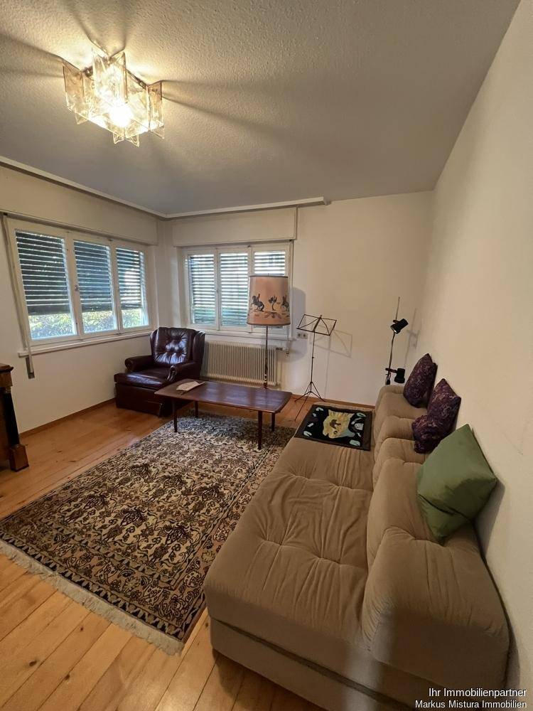 Helles Wohnzimmer mit beigem Sofa, Holzdielenboden und Blick ins Grüne.