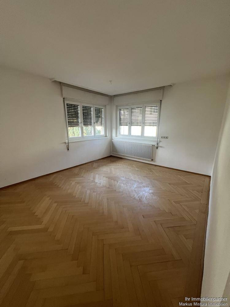 Helles Zimmer mit Fischgrätparkett und großen Fenstern, ideal für Wohn- oder Schlafbereich.