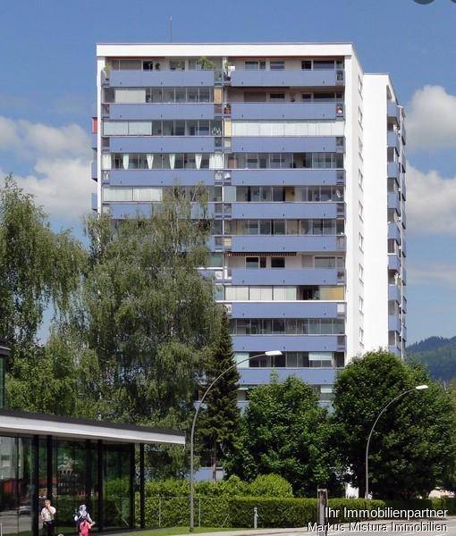 Ansicht des Mehrfamilienhauses mit zahlreichen Balkonen und umliegender Vegetation.