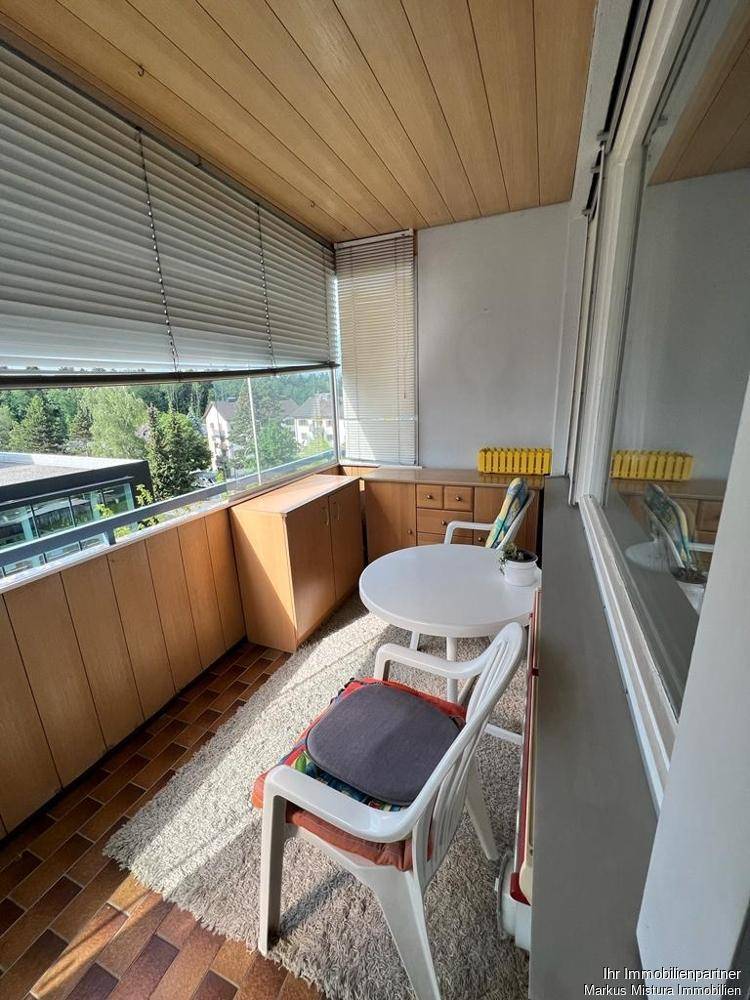 Verglaster Balkon mit Holzelementen, Fliesenboden und Sitzgelegenheiten mit Ausblick.