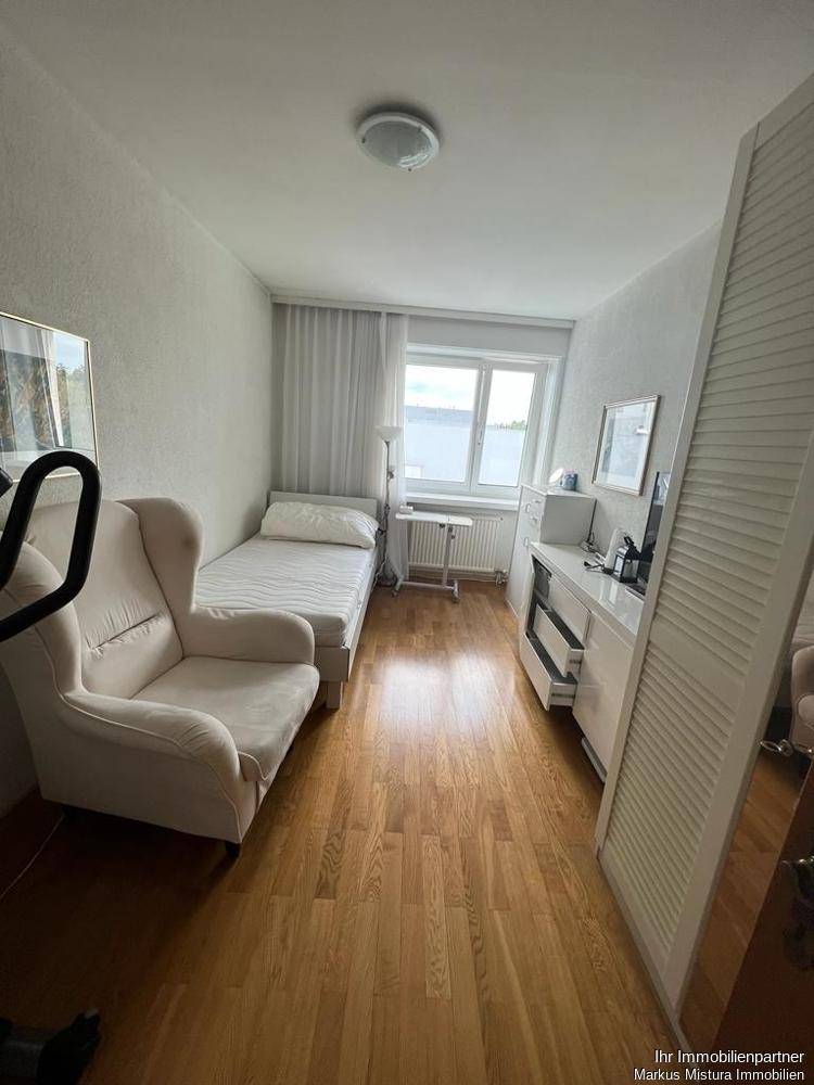 Gemütliches Schlafzimmer mit Holzfußboden, Einzelbett und einem bequemen Sessel.