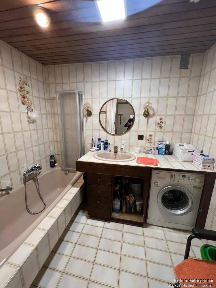 Badezimmer mit rosa Badewanne, weißen Fliesen, Holzdecke und Waschmaschine.