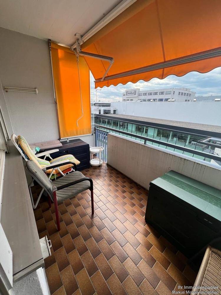 Balkon mit orangefarbener Markise, Fliesenboden und bequemen Gartenmöbeln.