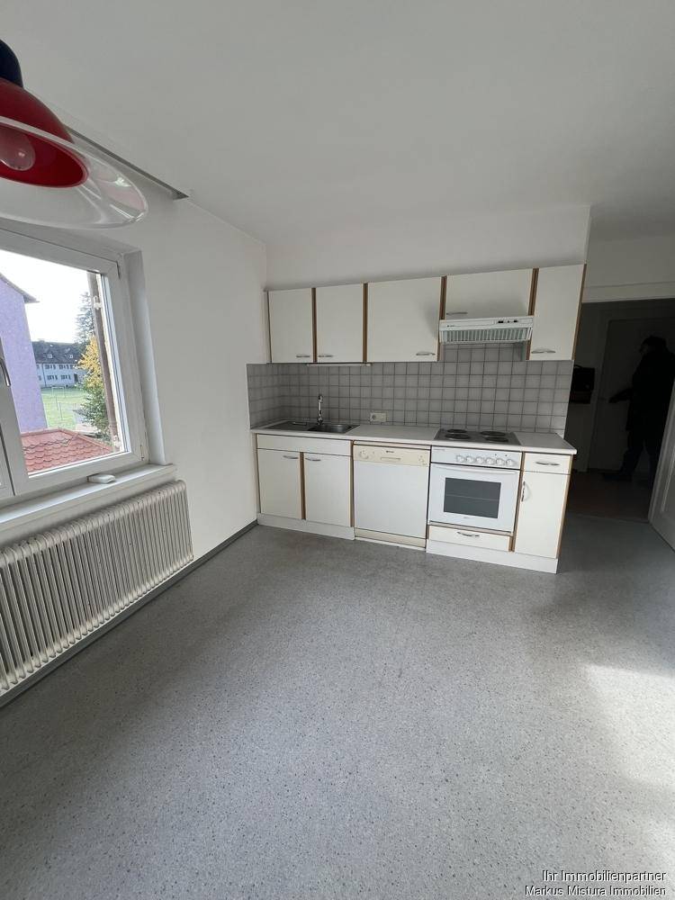Einfache Küche mit weißen Schränken, Herd, Spüle und Fenster.