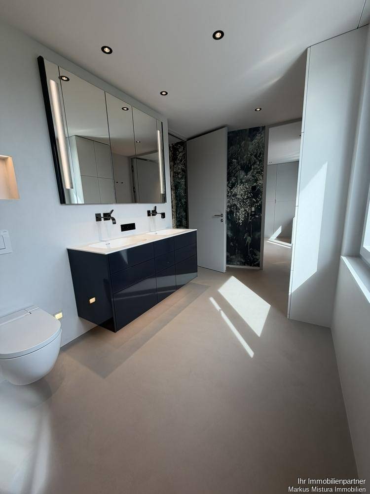 Geräumiges Badezimmer mit Doppelwaschbecken, großem Spiegelschrank und Zugang zu weiteren Räumen.