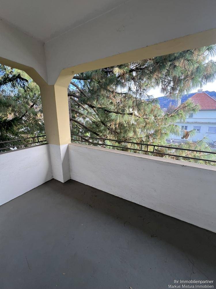 Überdachter Balkon mit Blick auf grüne Bäume und entfernte Berge, ideal zum Entspannen.