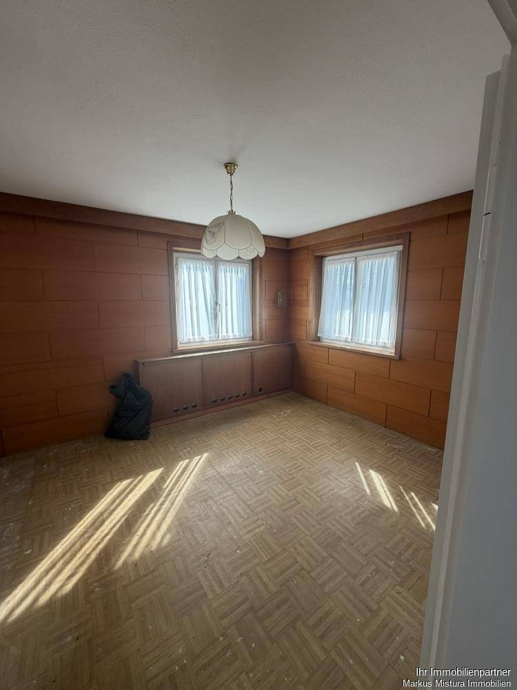 Schlafzimmer mit Holzvertäfelung, Parkettboden und zwei Fenstern, die viel Licht hereinlassen.