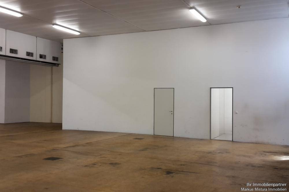 Leere Lagerhalle mit zwei Türen in einer weißen Wand und industrieller Beleuchtung an der Decke.