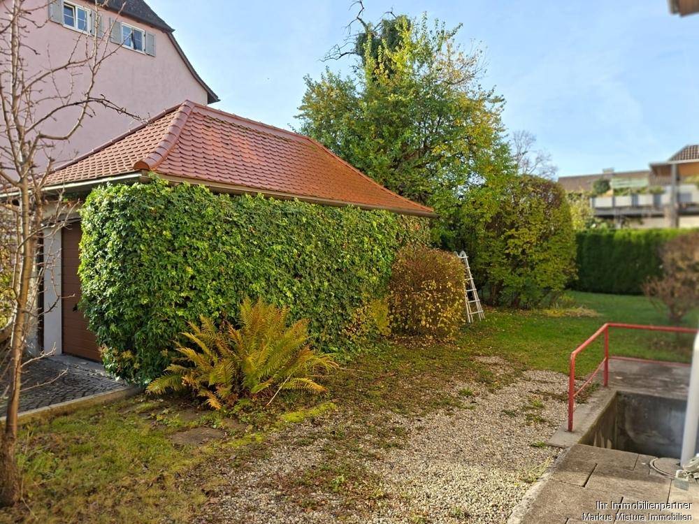 Grüne Gartenfläche mit einer von Efeu bewachsenen Garage und einem Kiesweg.