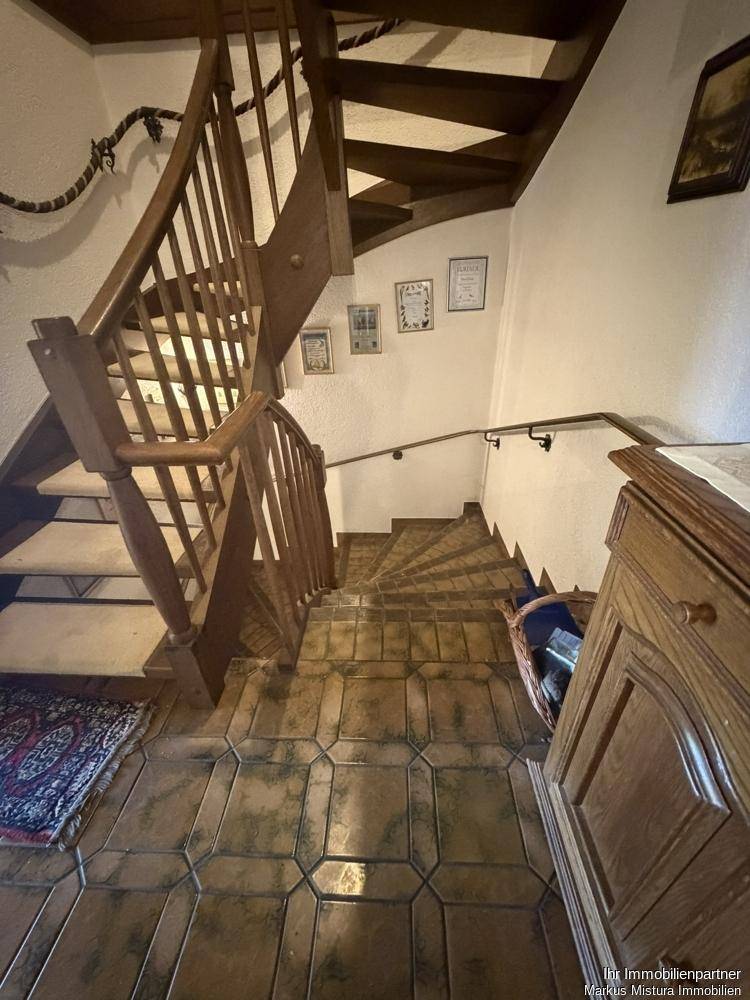 Holztreppe mit Fliesenstufen und traditionellem Geländer in einem Flur.